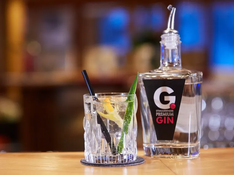Glas mit Gin und Zitrusgarnitur neben einer Flasche G Premium Gin auf einer Bar
