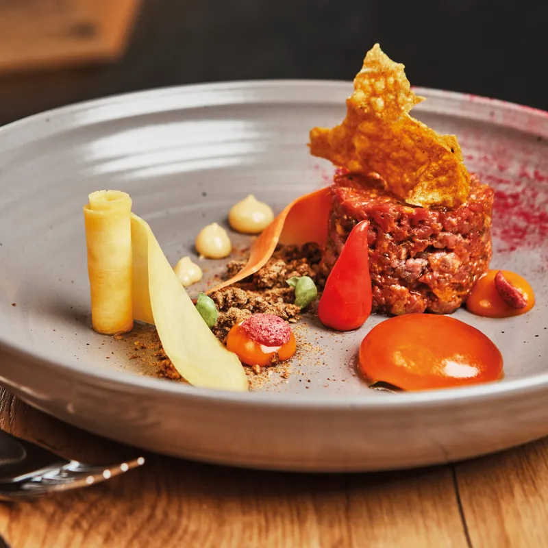 Gourmet beef tartare with vegetable garnish elegantly plated on grey dish