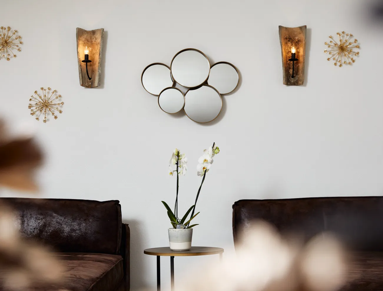 Modern living room with brown sofas, orchid plant, round wall mirrors and gold wall decor
