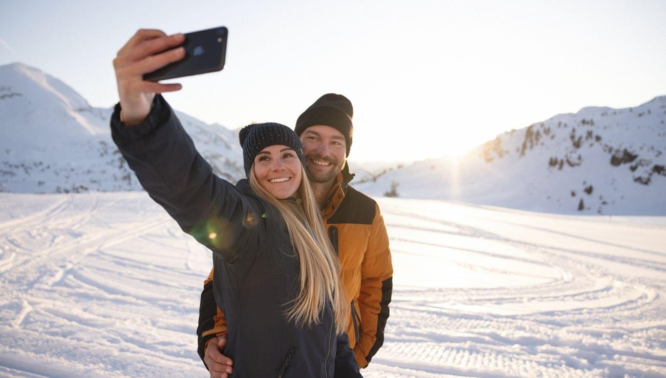Lächelndes Paar macht Selfie auf verschneitem Berg bei Sonnenuntergang