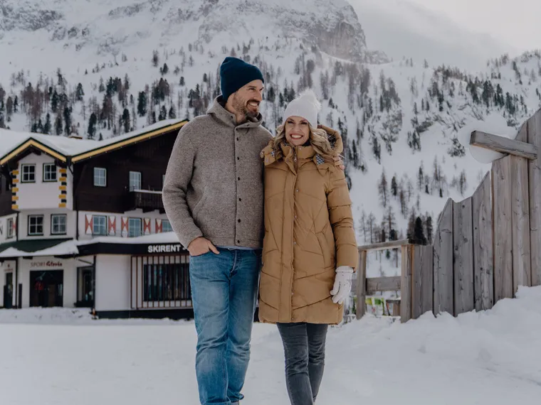 Couple walking in winter clothing through snowy alpine ski resort
