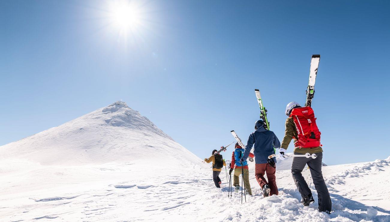 Gruppe von Skifahrern steigt bei Sonnenschein einen verschneiten Berg hinauf