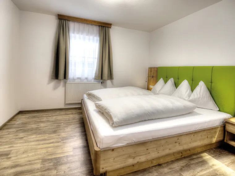 Modernes Hotelzimmer mit Doppelbett, grünem Kopfteil, Holzmöbeln und natürlichem Licht
