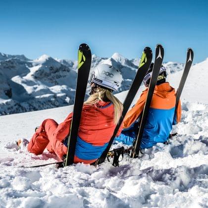 Skifahrer ruhen auf verschneiter Piste mit Skiern in Alpenlandschaft