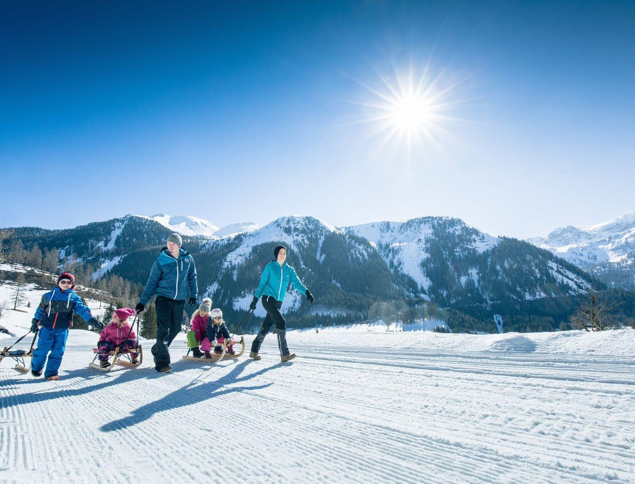 Familie wandert mit Schlitten im sonnigen Winterurlaub in den verschneiten Alpen