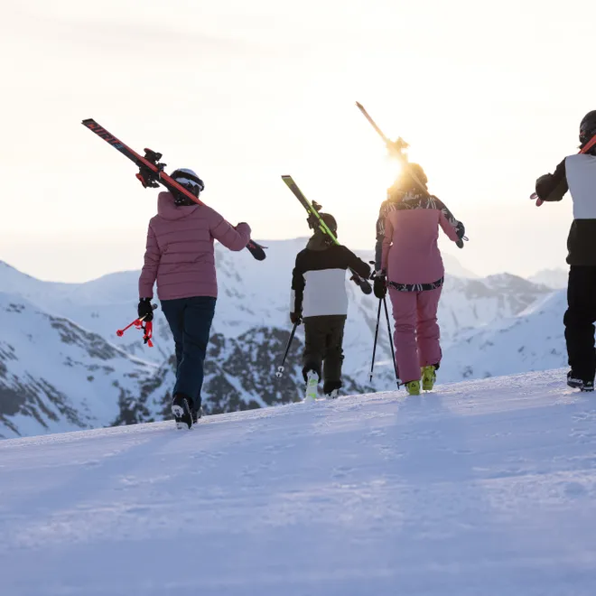 Skiers carrying skis at sunset on snowy mountain ridge