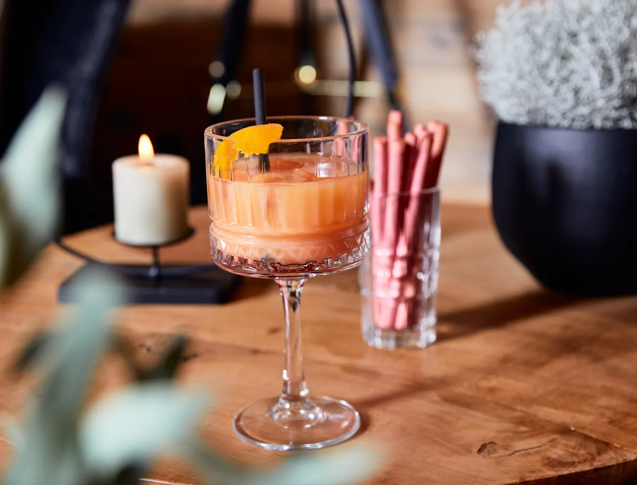 Serviertes Cocktailglas mit Orangendrink und Eiswürfeln auf einem Holztisch