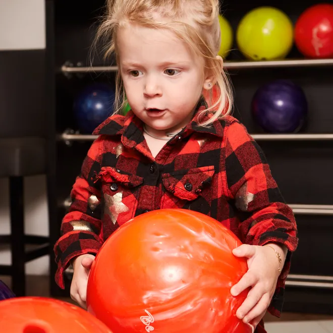 Young girl holding orange bowling ball at bowling alley