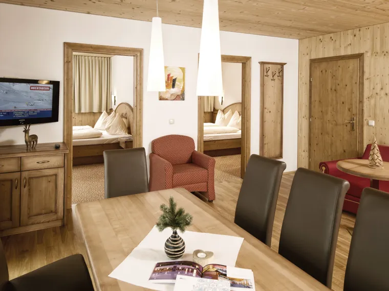 Cozy alpine hotel suite with wooden furniture, dining area, and two double bedrooms