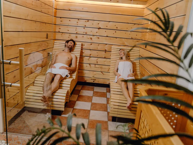 Relaxed couple laying on wooden loungers in wellness sauna room