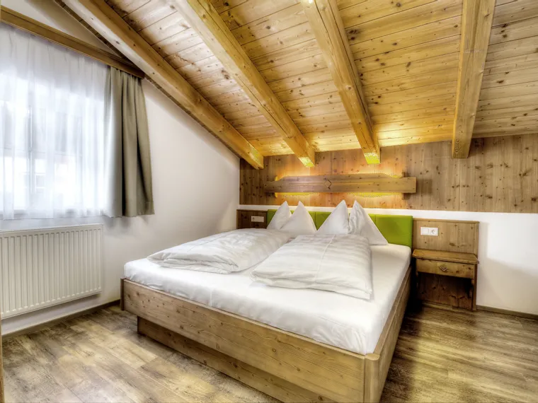Cozy alpine bedroom with wooden beams, double bed, and natural light from window
