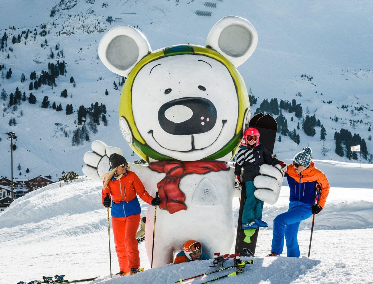 Family posing by giant bear mascot statue at snowy ski resort