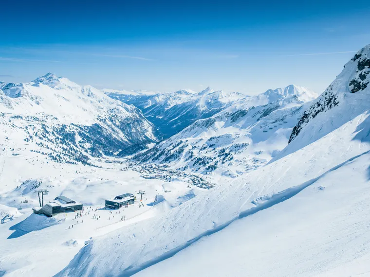 Snow-covered alpine ski resort with chair lifts and skiers under a clear blue sky