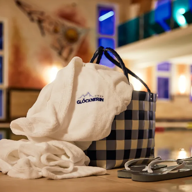 Wellness-Bademantel mit Glocknerin-Logo neben Korb und Flip-Flops am Innenpool