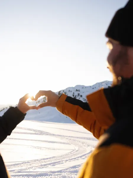Couple making heart shape with hands against snowy mountain sunset