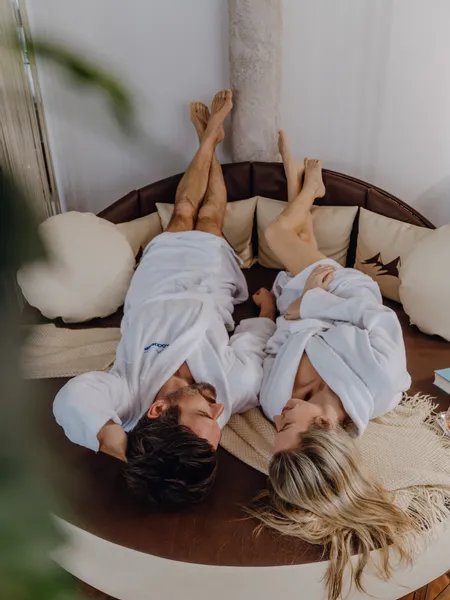 Couple in white bathrobes relaxing on round spa lounge bed