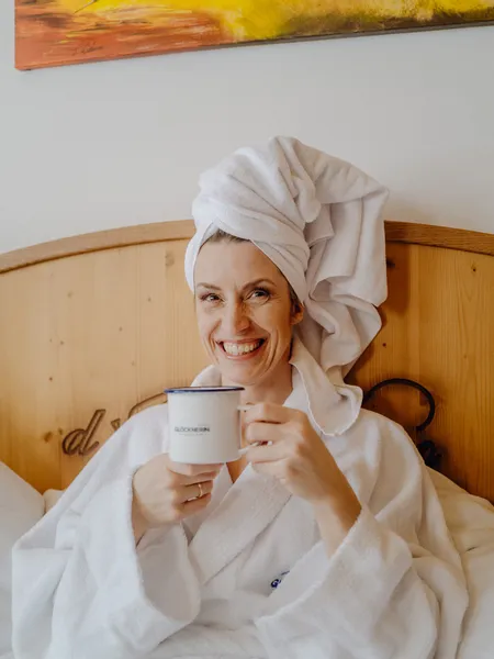 Smiling woman in bathrobe holding coffee mug in hotel bed