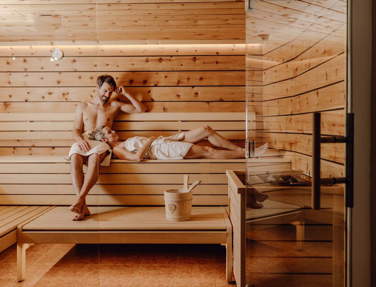 Couple relaxing together in a wooden sauna with soft warm lighting