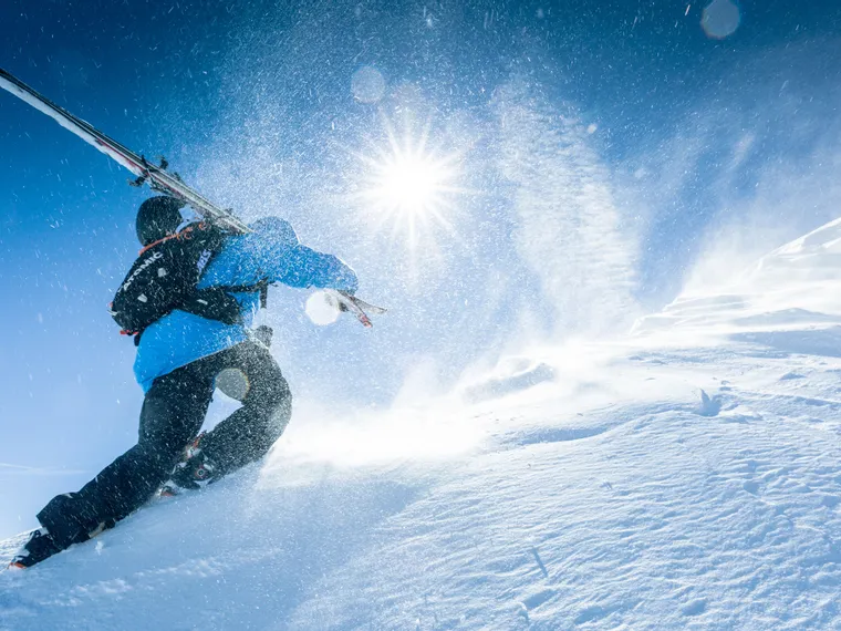 Skifahrer mit Ausrüstung wandert durch tiefen Pulverschnee bei strahlendem Sonnenschein