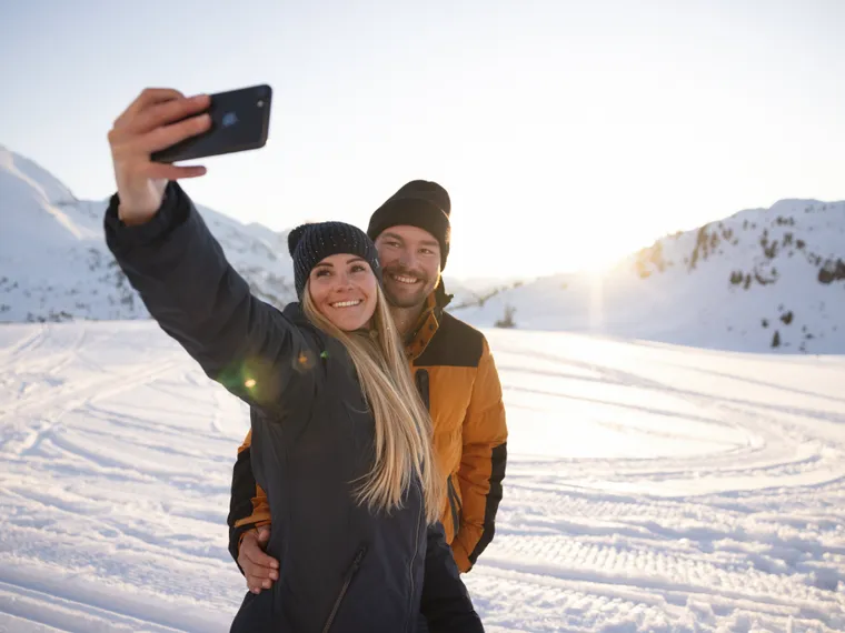 Lächelndes Paar macht Selfie auf verschneitem Berg bei Sonnenuntergang