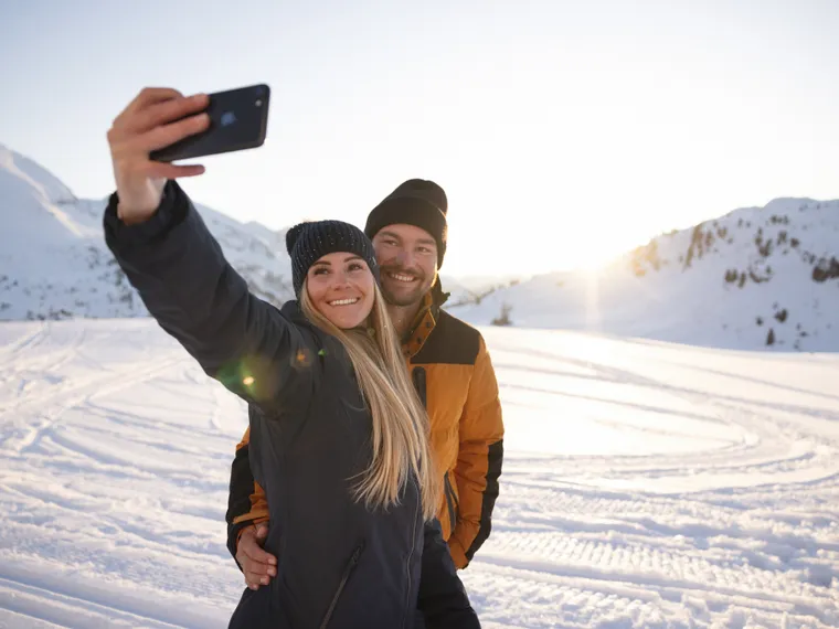 Smiling couple taking selfie on snowy mountain during sunset