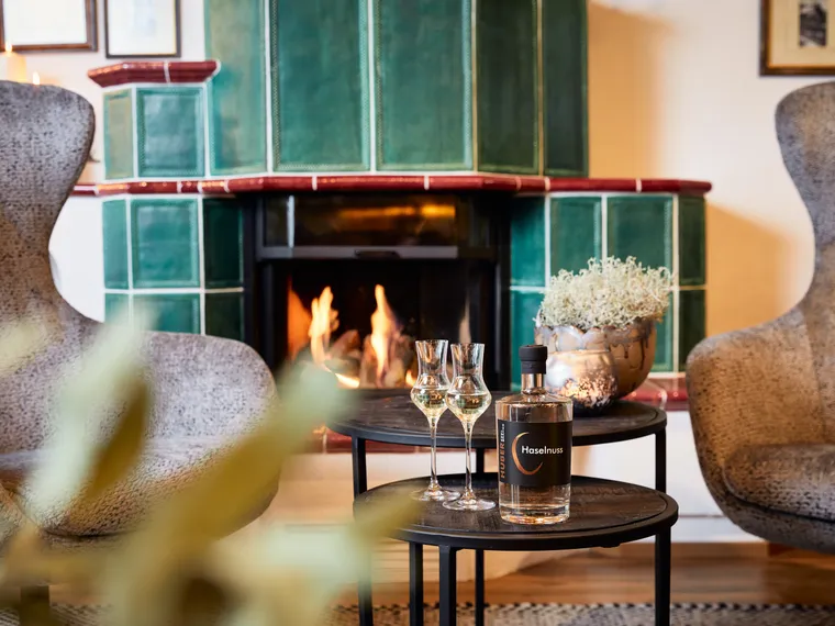 Haselnusslikör und Gläser auf Tisch vor grün gefliestem Kamin