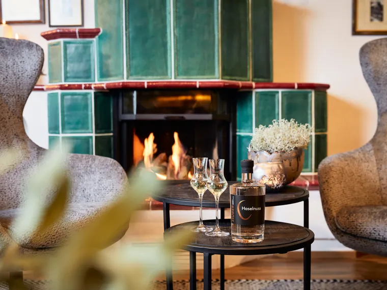 Hazelnut liqueur and glasses on table in front of green tiled fireplace