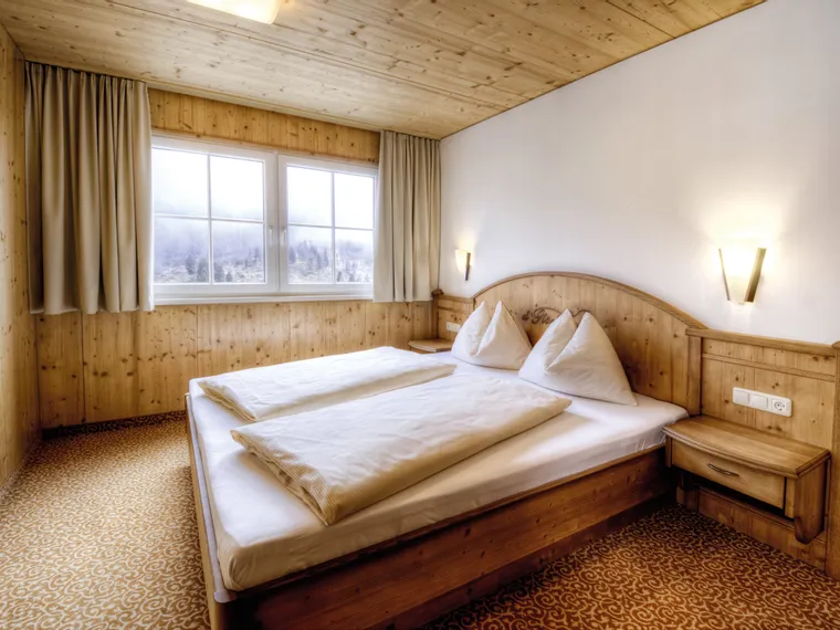Cozy alpine hotel room with wooden furniture, double bed, and mountain view