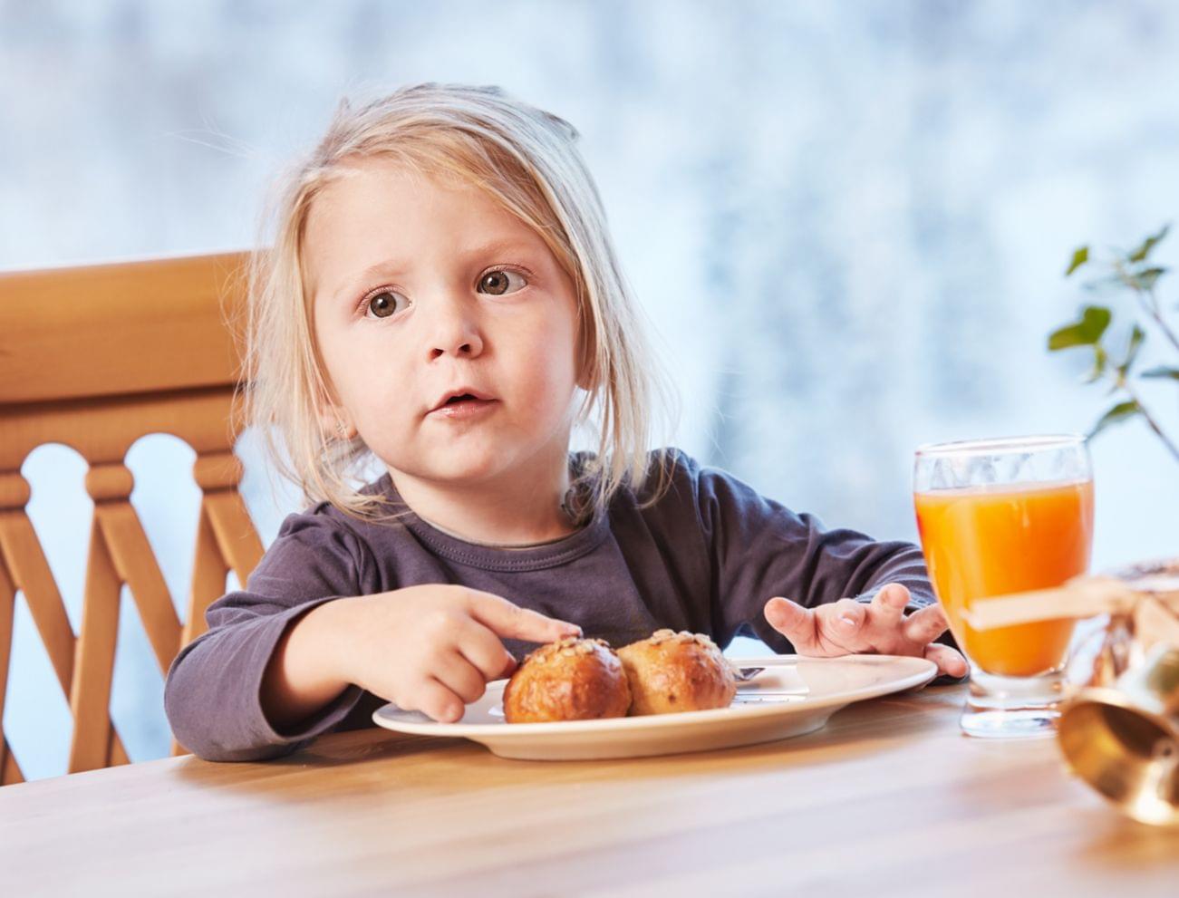 Young child eating pastry and drinking orange juice at breakfast table