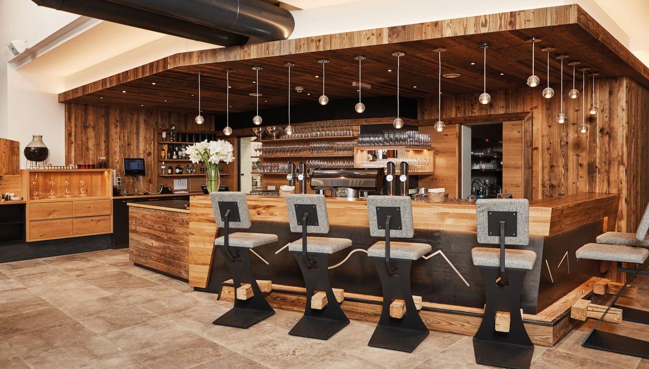 Moderne Bar im rustikalen Stil mit Holzverkleidung, Hängelampen und gepolsterten Barhockern