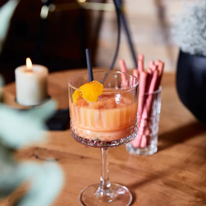 Cremiger orangefarbener Cocktail mit Orangenschale auf Holztisch