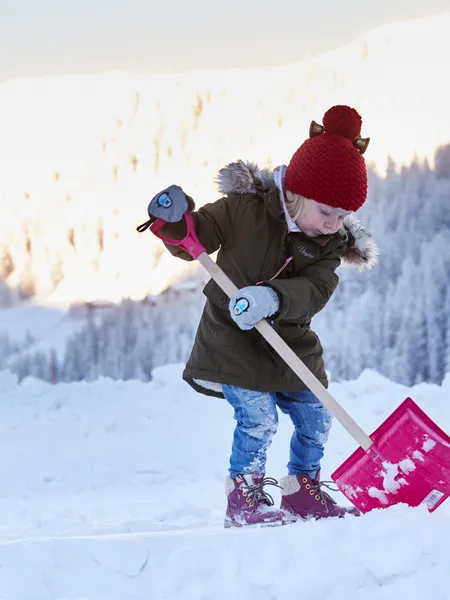 Kind mit roter Mütze schaufelt Schnee in winterlicher Berglandschaft