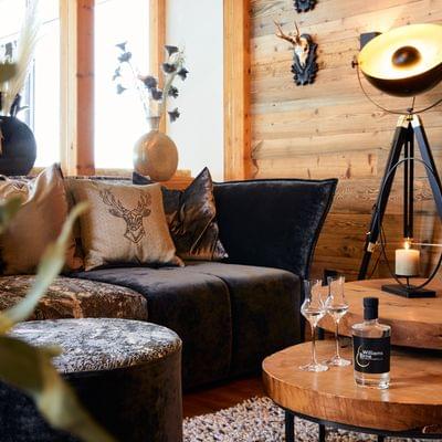 Gemütliches Wohnzimmer im Alpenstil mit schwarzem Samtsofa, Zierkissen, rustikalen Holzakzenten und Stehlampe