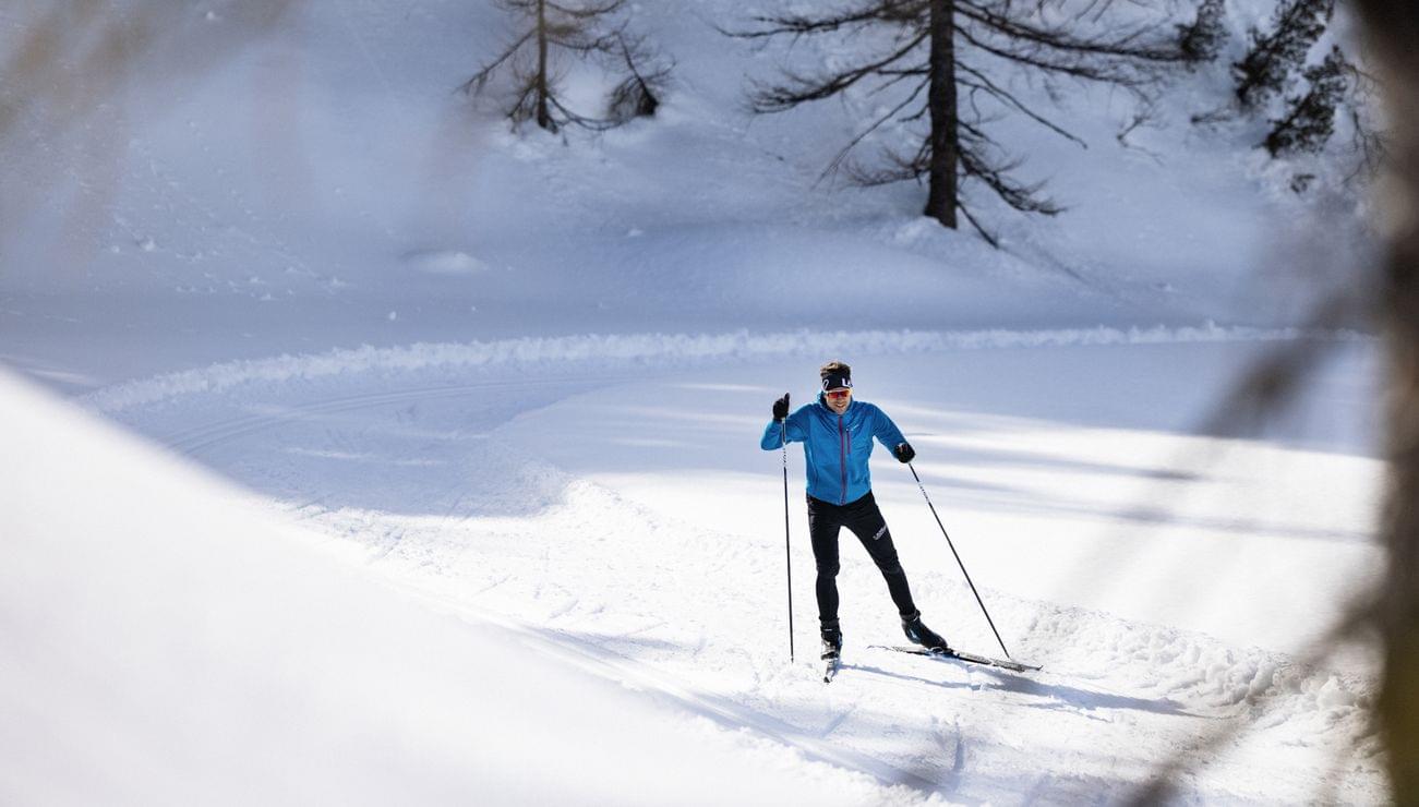 Langläufer in winterlicher Waldlandschaft auf schneebedeckter Loipe