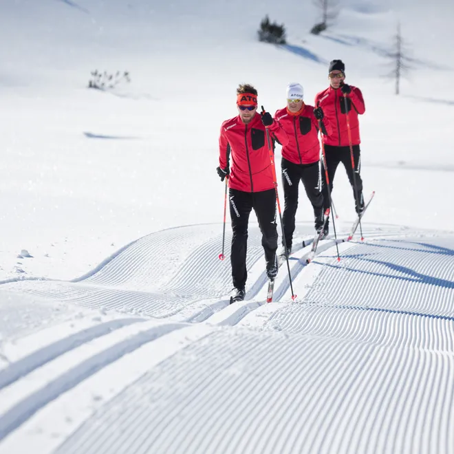 Three cross-country skiers in red jackets gliding on groomed snow trail