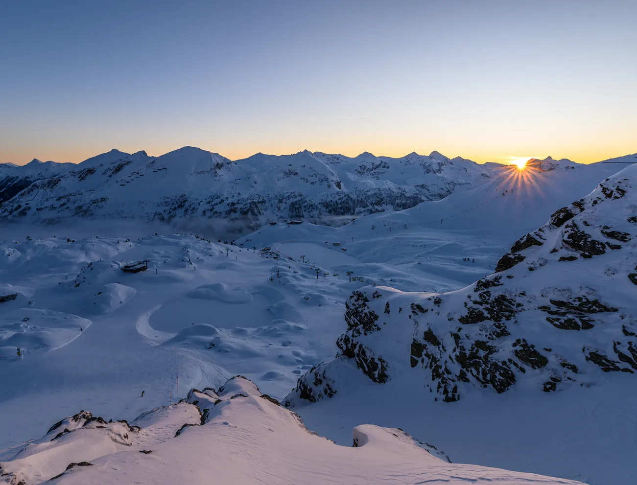 Winterlicher Sonnenaufgang über schneebedeckten Alpen und Skipisten
