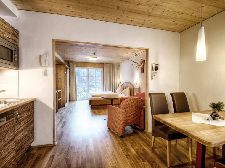 Cozy wooden apartment interior with kitchenette, dining area, and bedroom with natural light