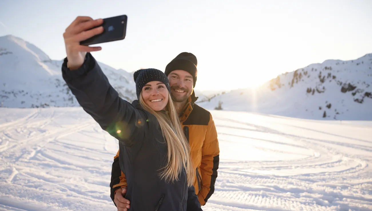 Lächelndes Paar macht Selfie auf verschneitem Berg bei Sonnenuntergang