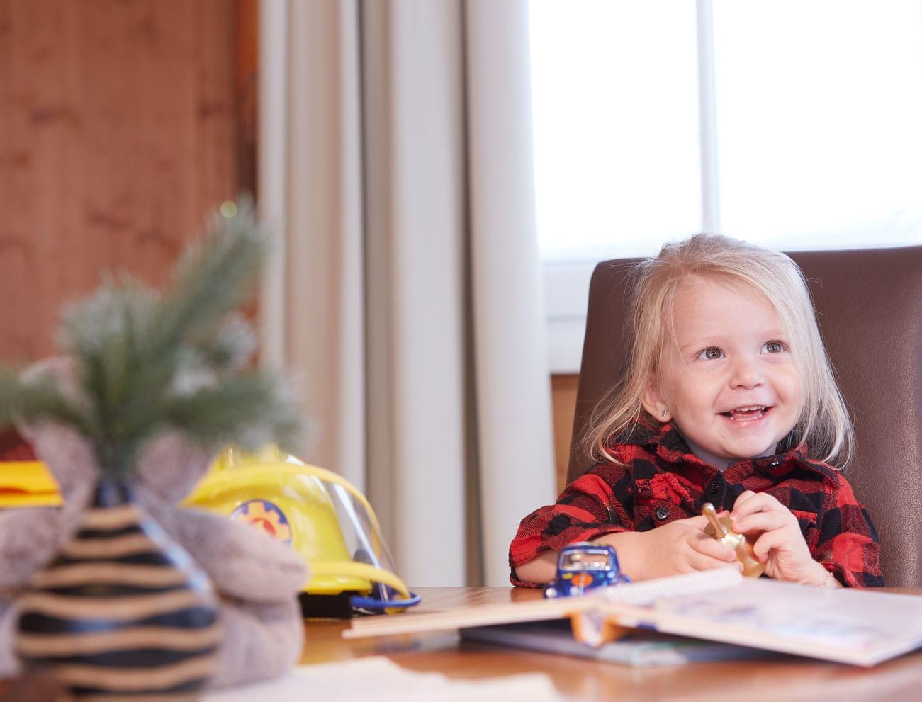 Lächelndes kleines Mädchen am Tisch mit Spielzeug und Kinderbuch
