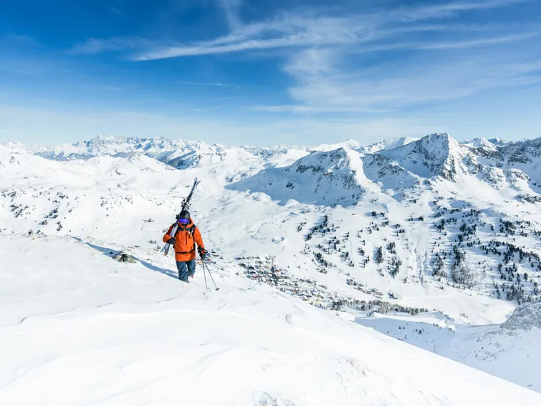 Skier hiking through snowy alpine mountains under clear blue sky
