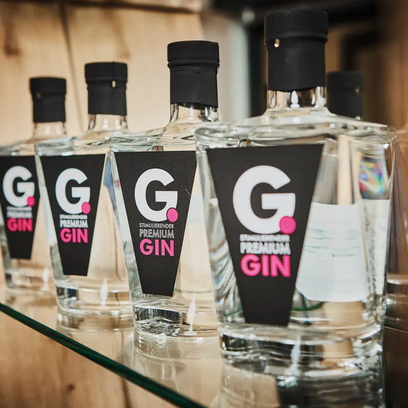 Reihe von G. Premium Gin Flaschen mit schwarzem Etikett auf einem Glasregal