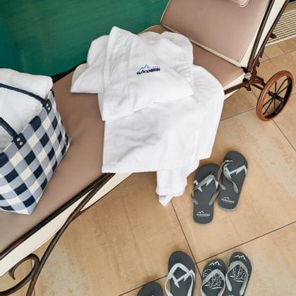 Poolside spa chair with Glöcknerin robe, checkered bag, and branded flip-flops on tile floor