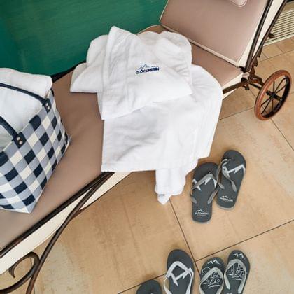 Wellnessliege am Pool mit Glöcknerin-Bademantel, kariertem Korb und Hausschuhen auf Fliesenboden