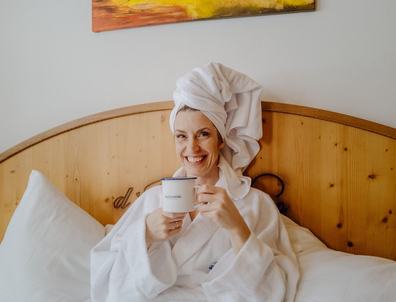 Smiling woman in bathrobe holding coffee mug in hotel bed