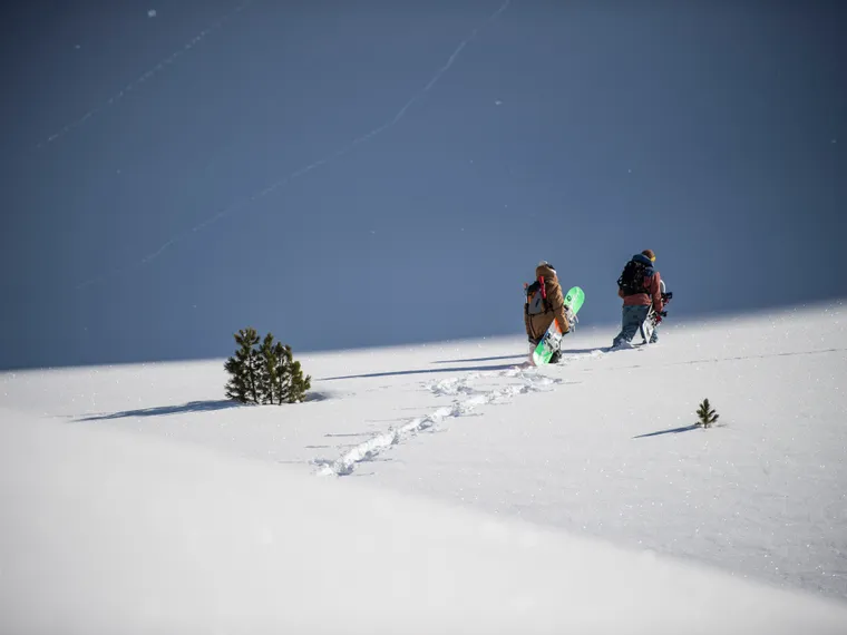 Two snowboarders hiking uphill through deep powder snow on a mountain