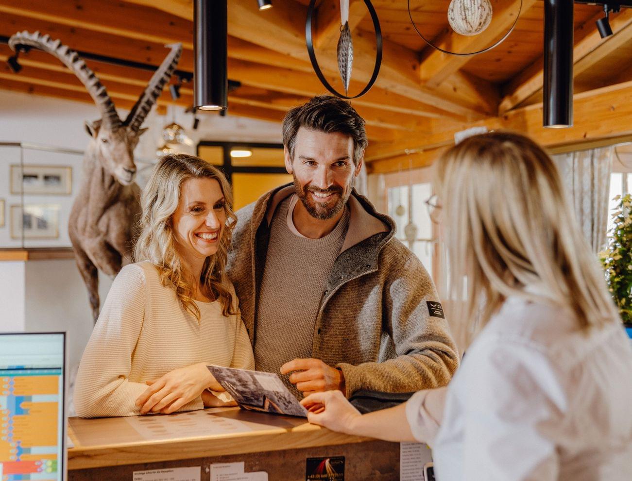 Lächelndes Paar am Hotelrezeptionstresen spricht mit der Rezeptionistin