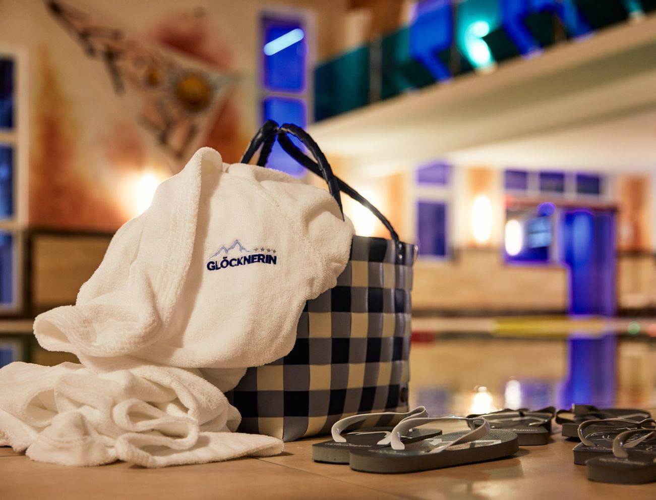 Wellness-Bademantel mit Glocknerin-Logo neben Korb und Flip-Flops am Innenpool