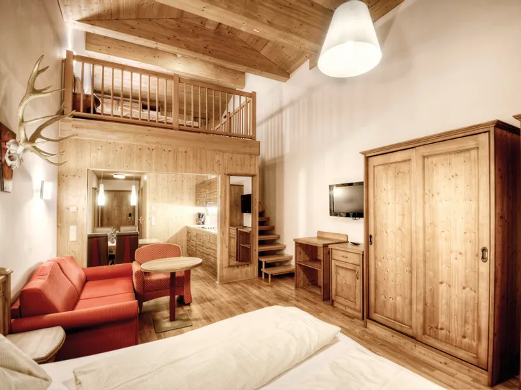 Cozy alpine hotel room with wooden furniture, loft bed, and red sofa set