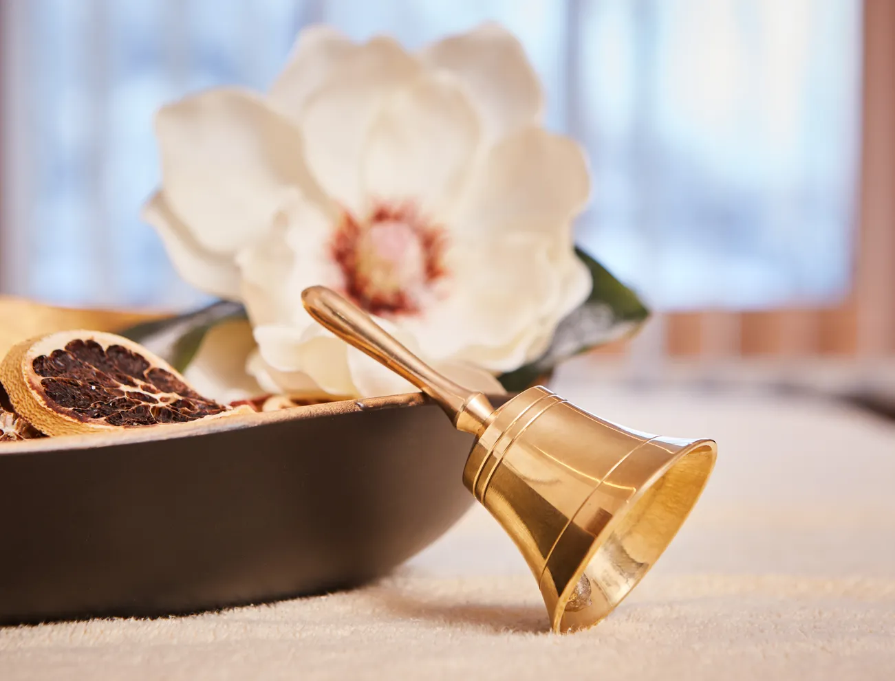 Golden bell next to dried citrus slices and white magnolia flower in a spa setting