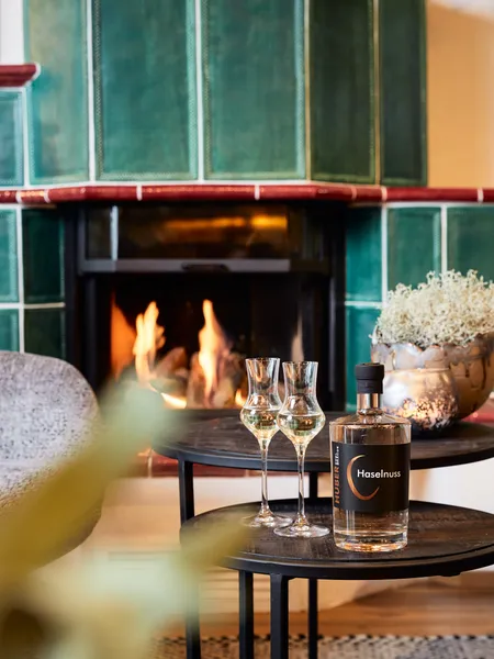 Hazelnut liqueur and glasses on table in front of green tiled fireplace